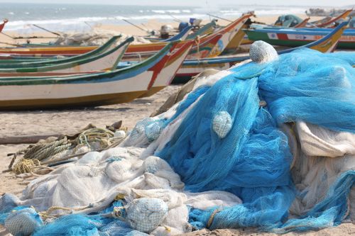 Free Piled fishing nets with colorful boats on a sunny beach in Andhra Pradesh, India. Stock Photo
