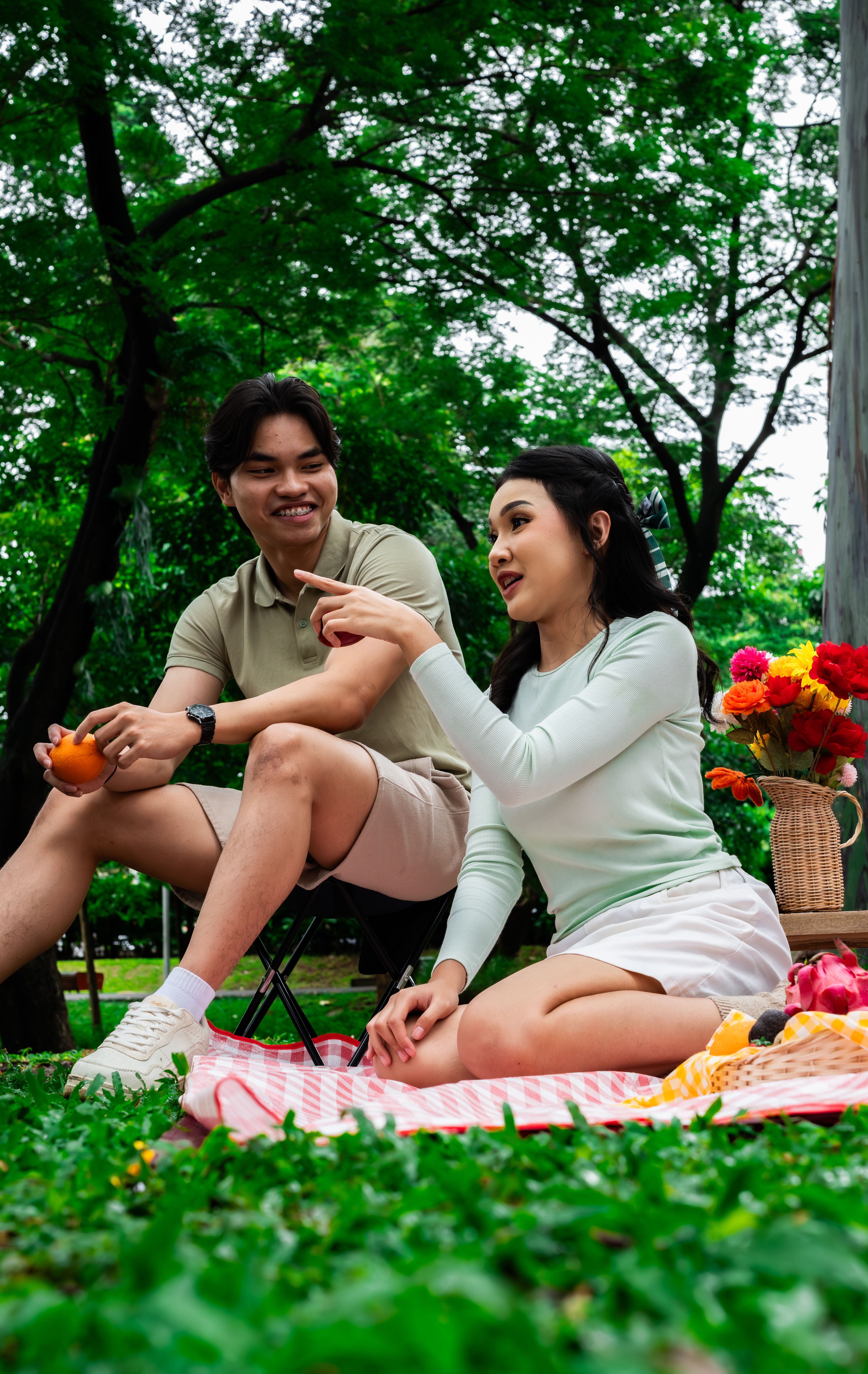 Asian couple enjoying a picnic in a lush Indonesian park, surrounded by nature and flowers.