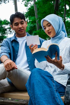 An Asian couple enjoying a relaxing reading session outdoors in a lush park setting.
