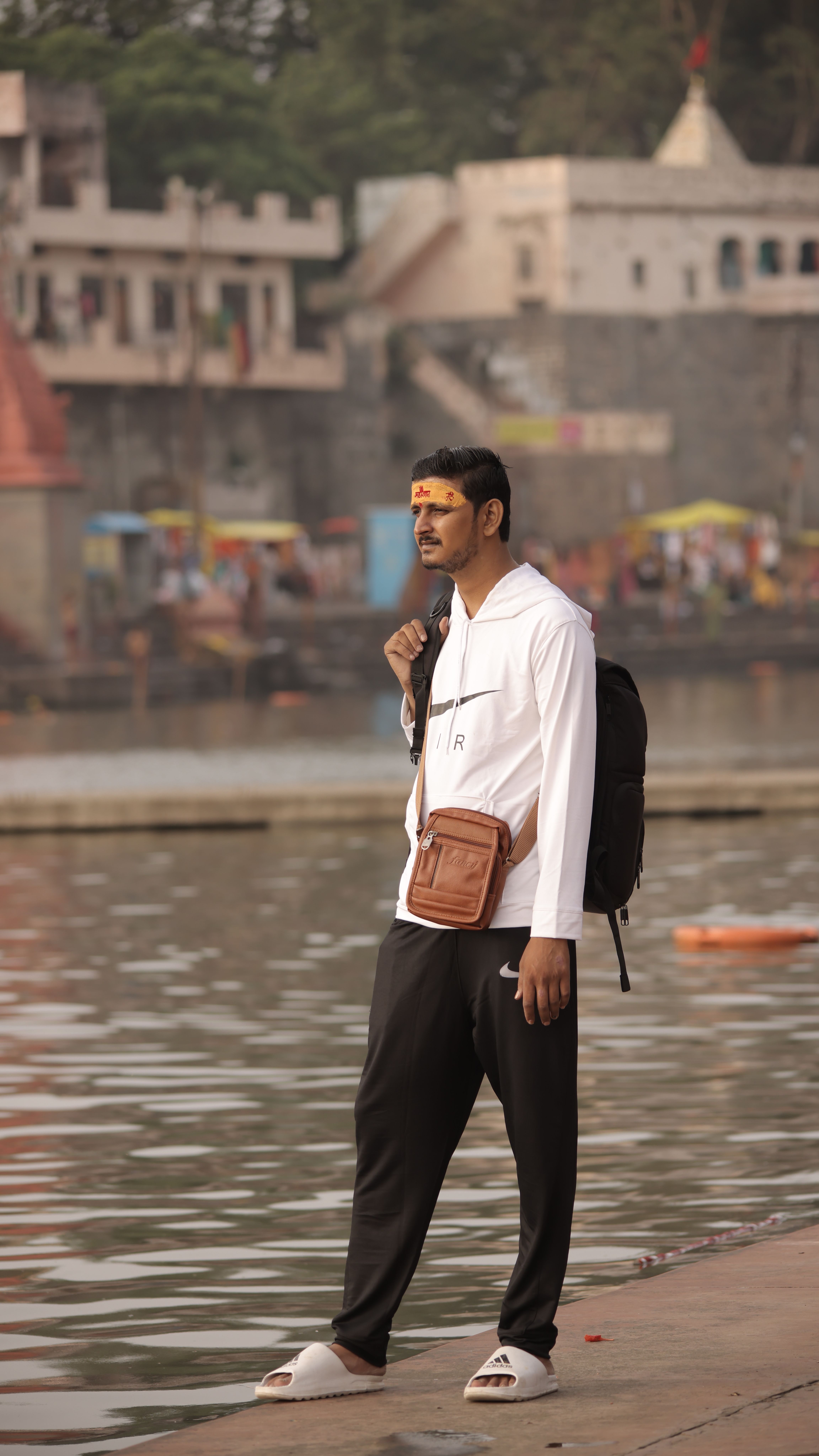 A man wearing casual clothing stands by a riverside in an urban setting.