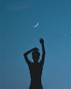 在新月下，晴朗的夜空中有个举手的人的剪影