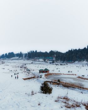 Scenic view of snowy landscape in Gulmarg, Kashmir, with people enjoying winter activities.
