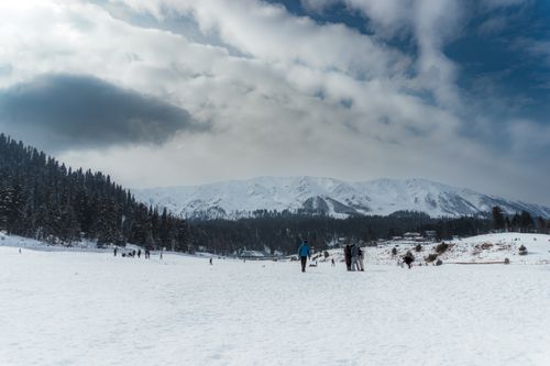 Free Breathtaking winter landscape of snow-covered Gulmarg with distant alpine mountains under a dramatic sky. Stock Photo