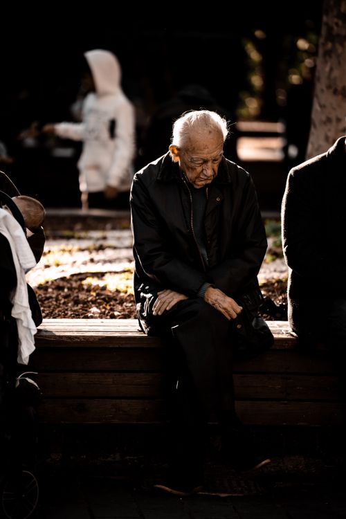 Free Elderly man sitting on a bench outdoors, deep in thought, during autumn. Stock Photo