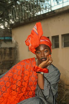 Stylish and contemplative woman in traditional African attire featuring vibrant orange colors. Perfect for fashion and cultural themes.
