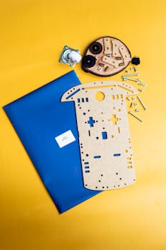 Flat lay of DIY robotics kit with gears and frame on a vibrant yellow surface.