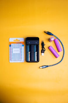 Top view of electronics kit with charger, batteries, and cables on vivid yellow backdrop.