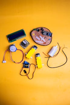 Assorted robotics components and circuit boards on a vibrant yellow surface, emphasizing innovation and technology.