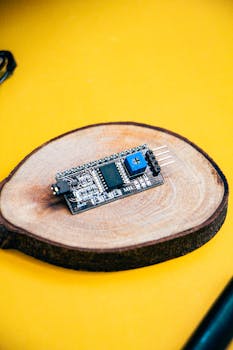 Close-up of a microcontroller on wood against a vivid yellow backdrop, showcasing modern electronics.