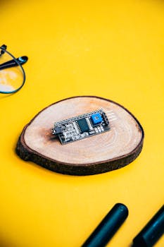 Microcontroller on a wooden slice with a vibrant yellow background, ideal for tech and electronics themes.