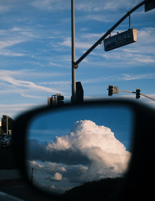 Free Dramatic sky and clouds reflected in car mirror with traffic light and street sign in view. Stock Photo