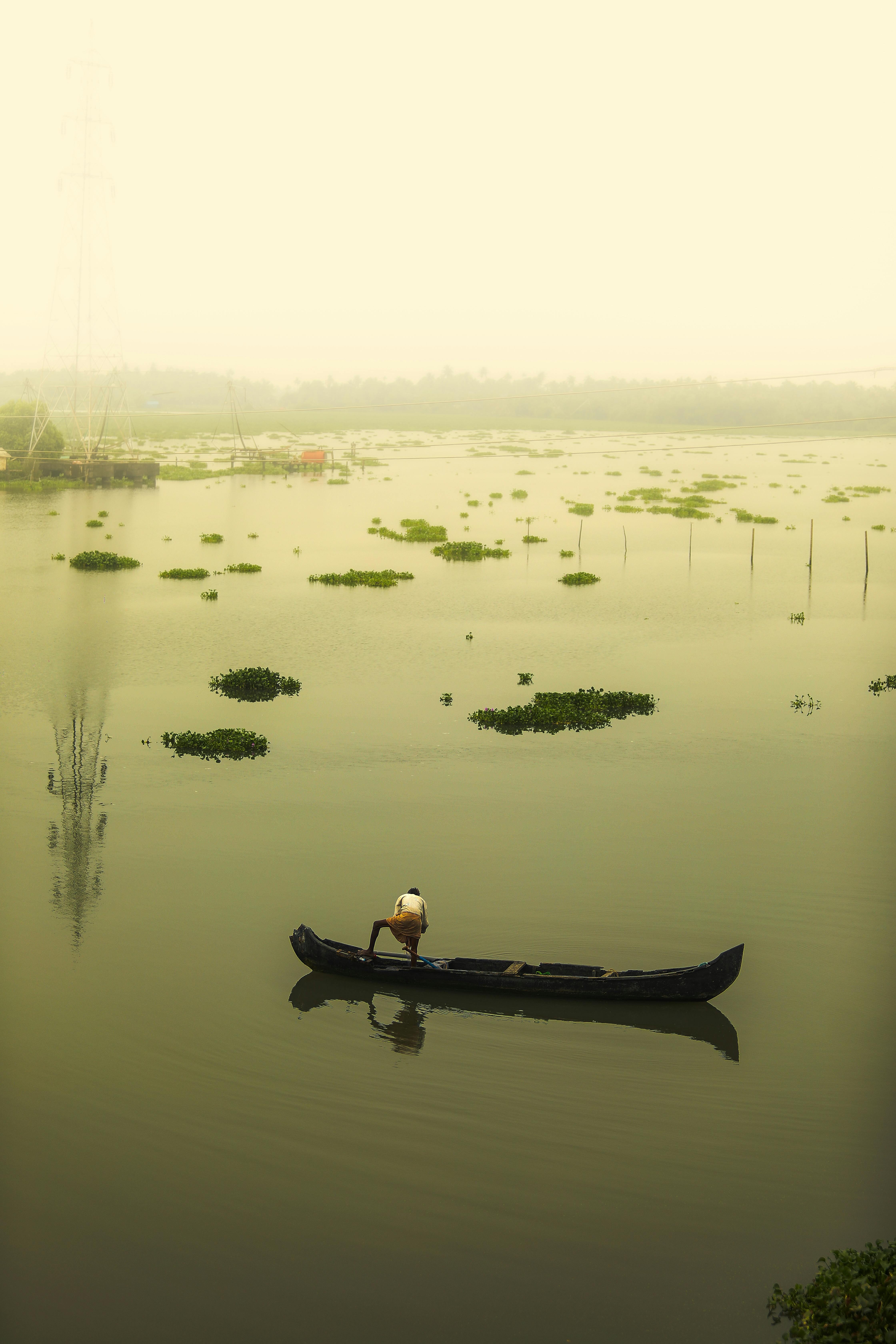 A solitary canoe on calm backwaters surrounded by greenery under a misty morning sky.