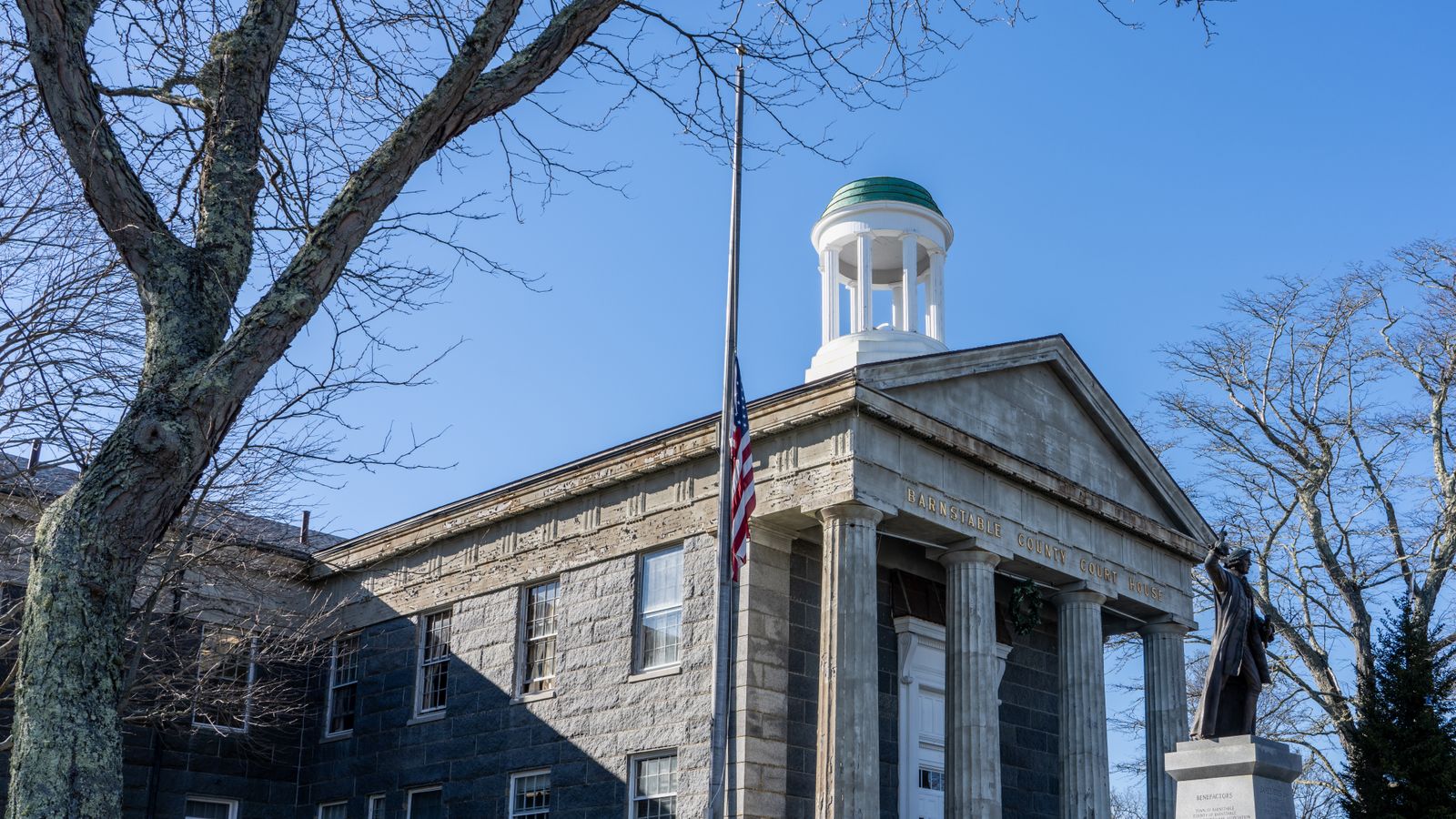 Front view of the historic Barnstable County Courthouse with a prominent statue and flag.