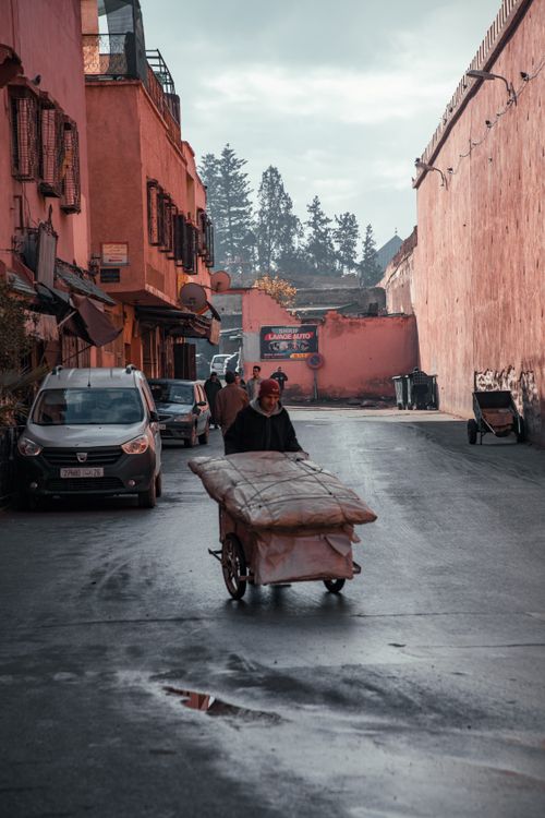 Free A man pushing a cart in the medina of Marrakesh, Morocco surrounded by traditional architecture. Stock Photo
