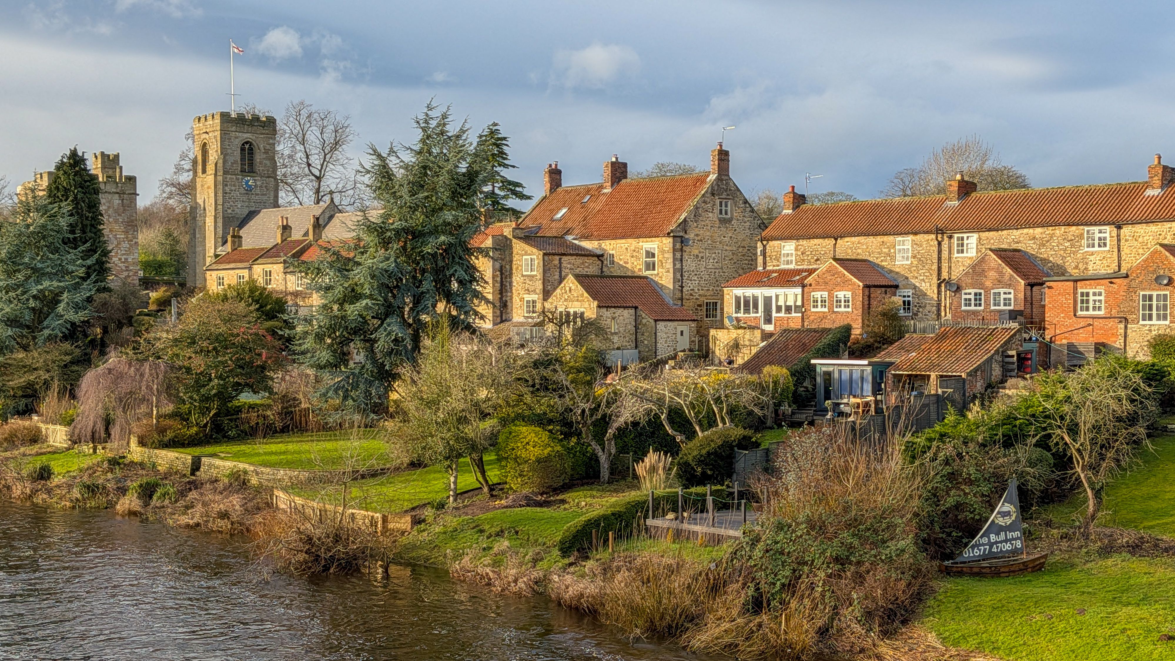 Picturesque view of West Tanfield's riverside with historic architecture and lush greenery.