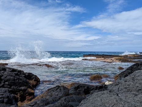 Waves crash against a rocky shore under a bright blue sky, showcasing coastal beauty.
