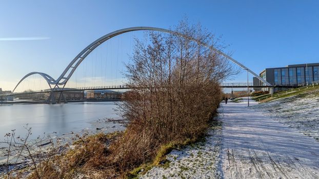 A serene winter view of the Infinity Bridge in Thornaby, England, with frosty paths and blue skies.