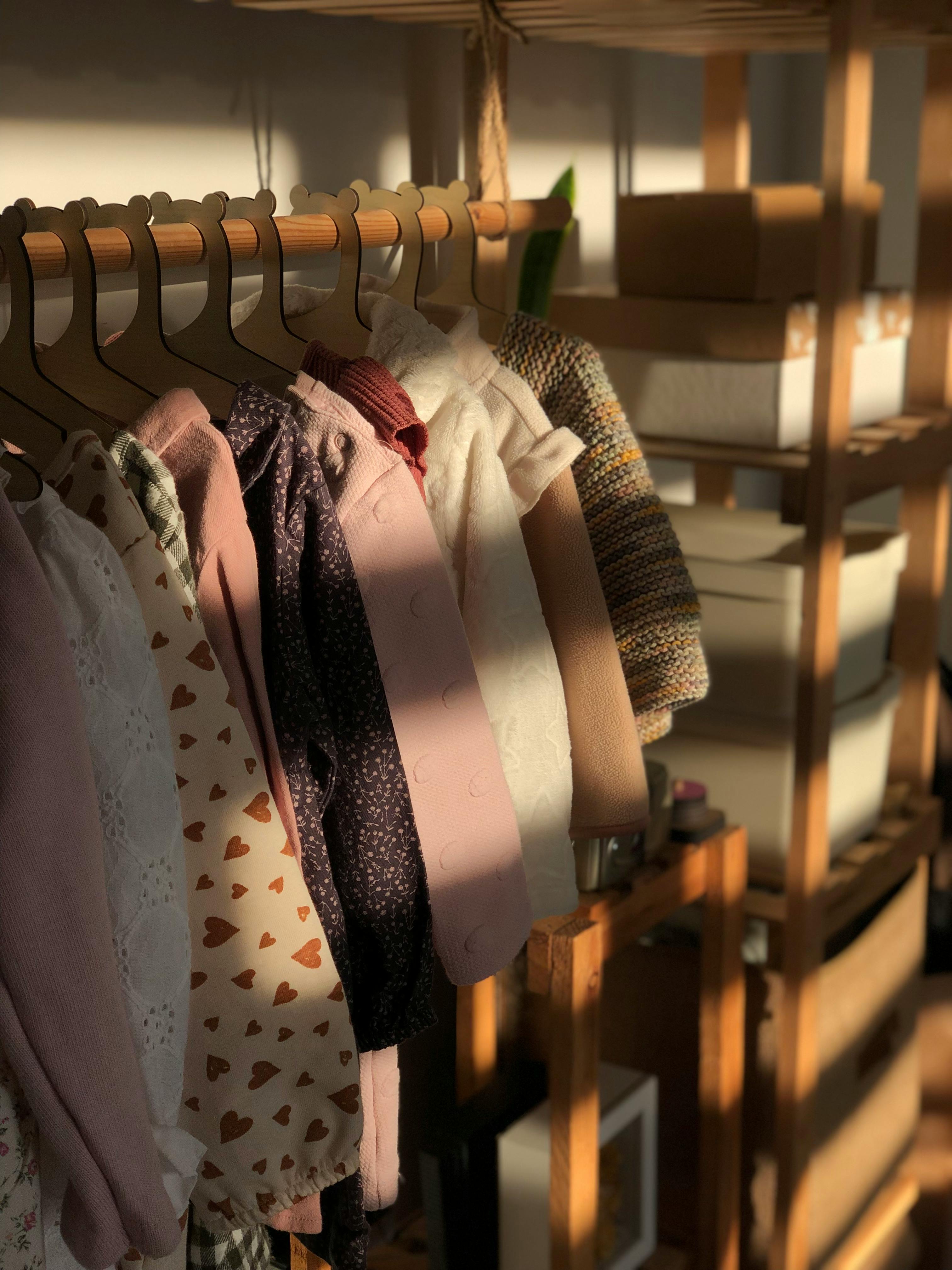 A selection of children's clothes hanging on wooden hangers in warm sunlight.