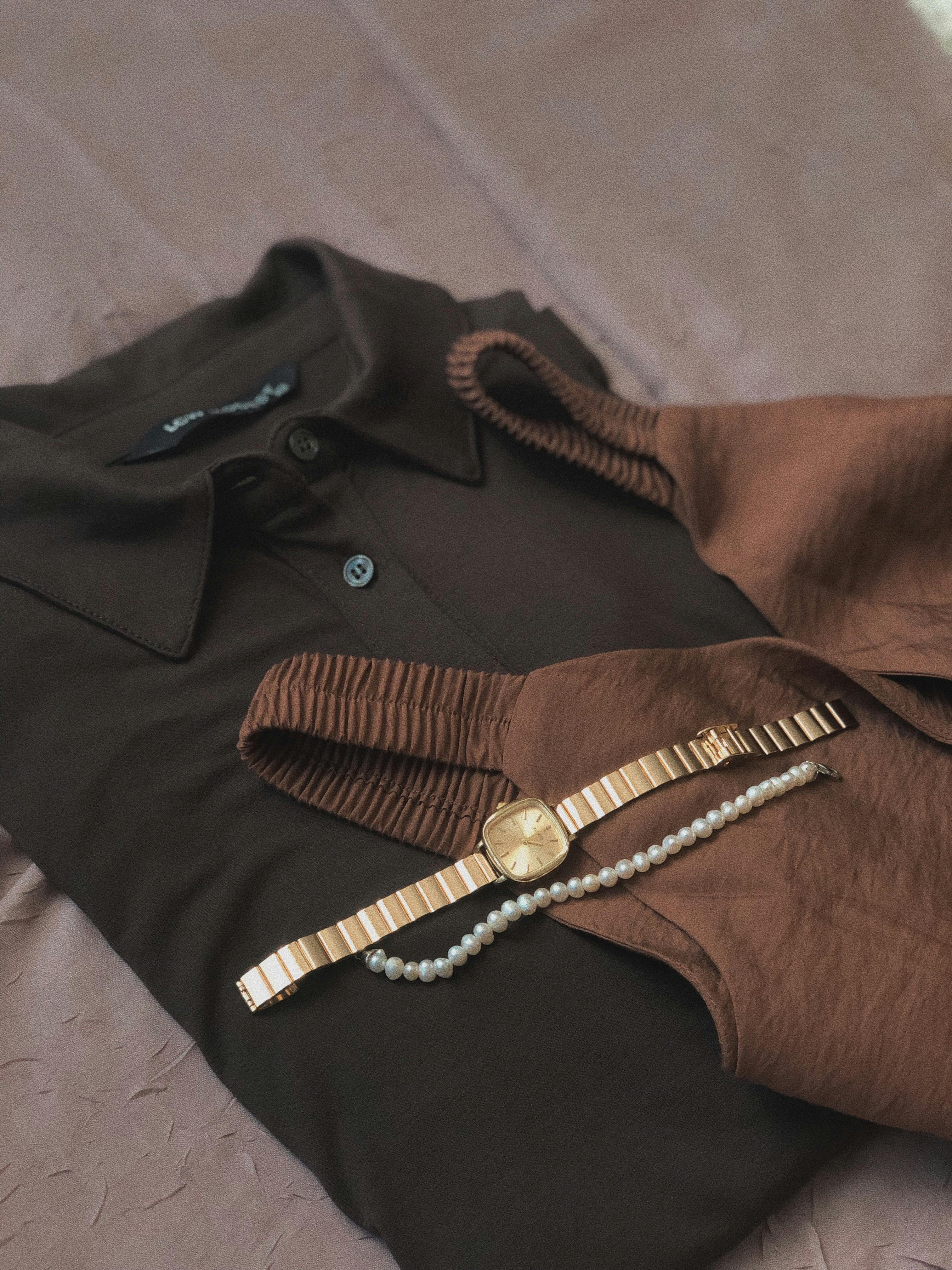 Elegant flat lay of brown shirt, top, gold watch, and pearl bracelet.
