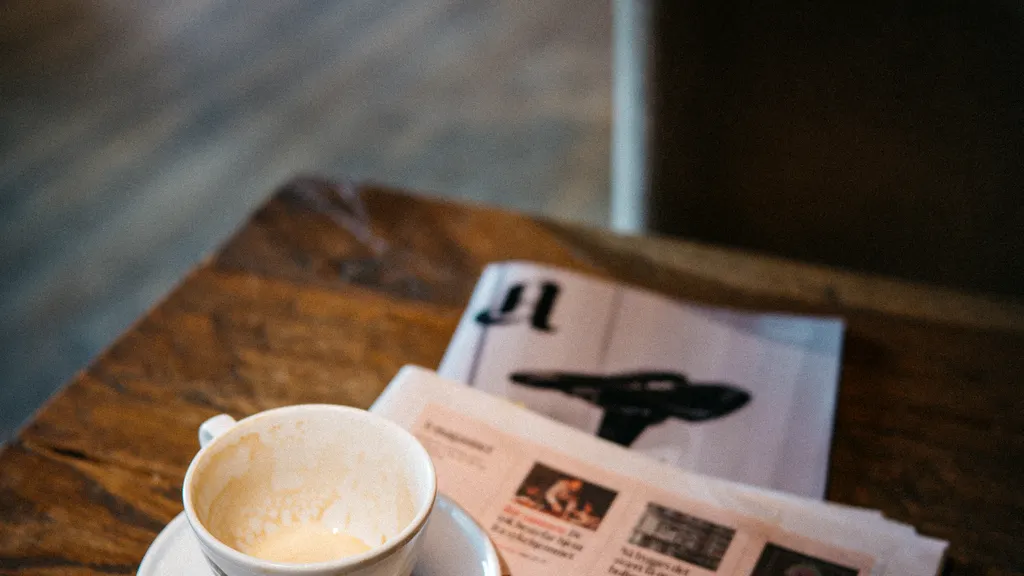 Coffee cup beside a newspaper on a wooden cafe table