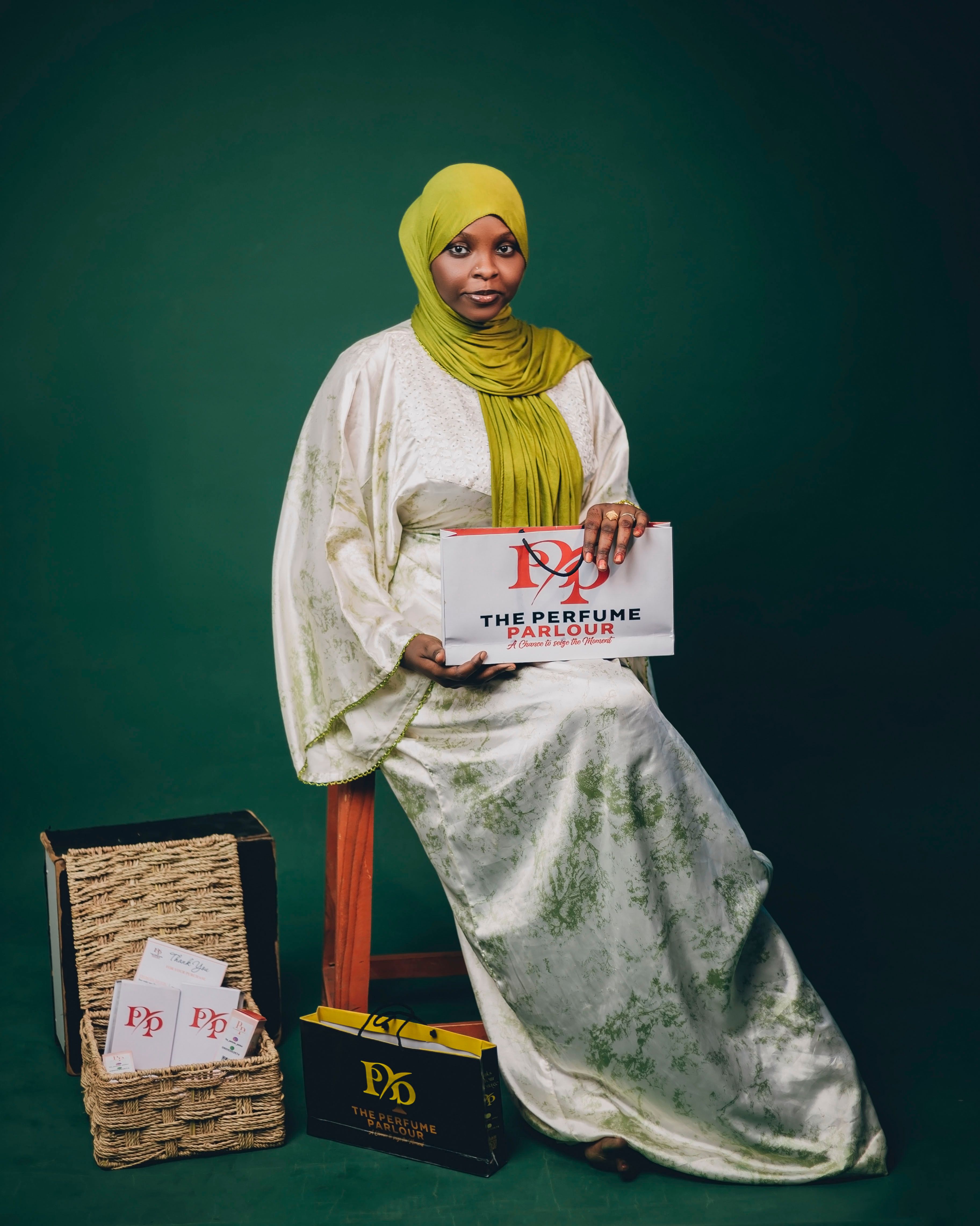 A woman in traditional attire holding a Perfume Parlor box against a green backdrop.