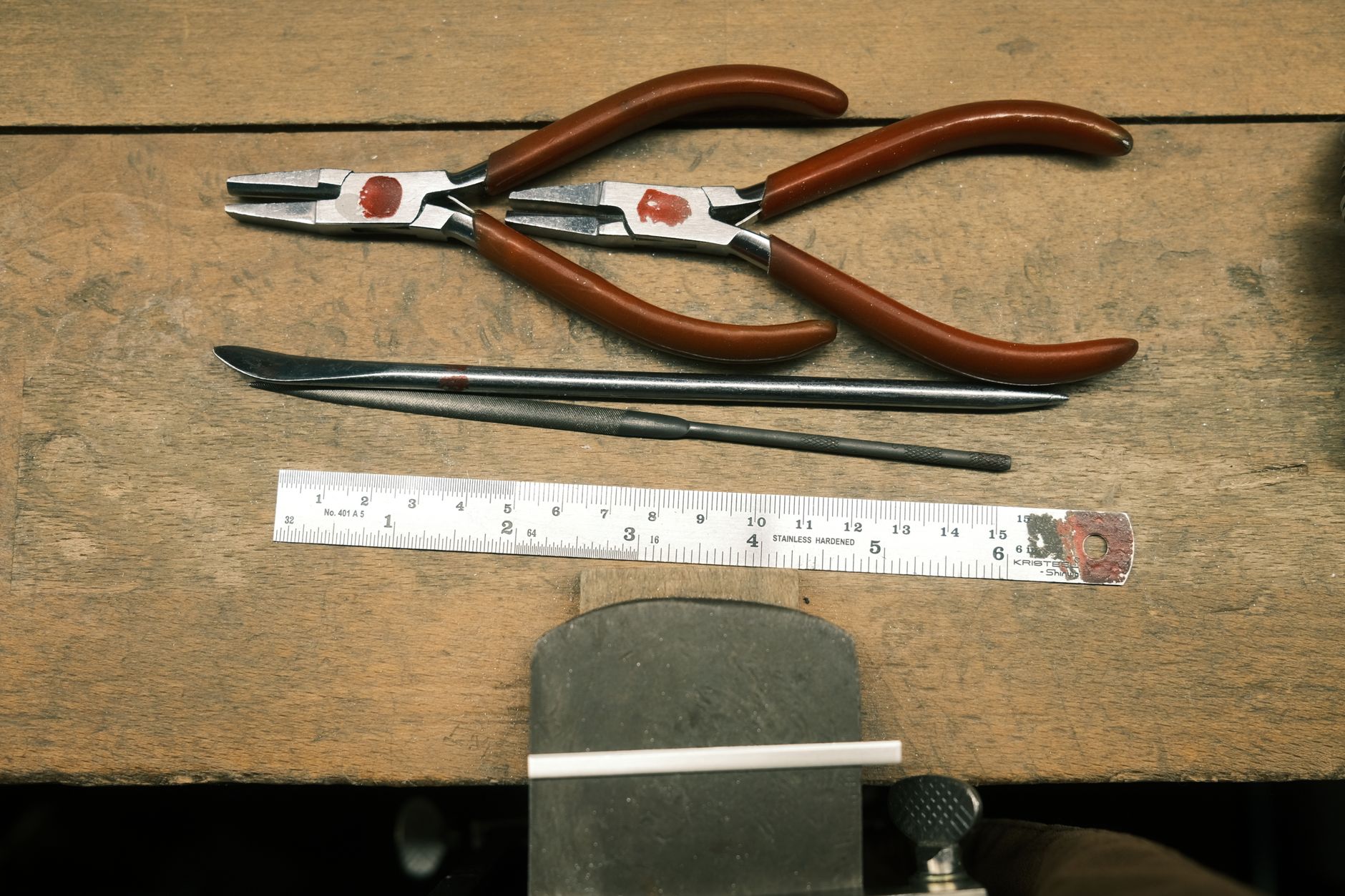 Flat lay of essential hand tools including pliers, file, and ruler on a wooden workbench.