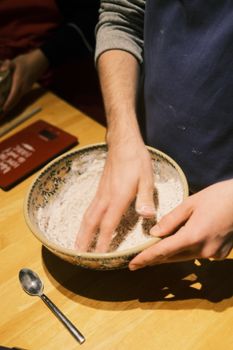 Person mixing dough in a ceramic bowl on a wooden table, emphasizing homemade baking.