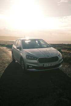 A silver car parked on a country road during sunset, highlighting the landscape with a visible license plate.