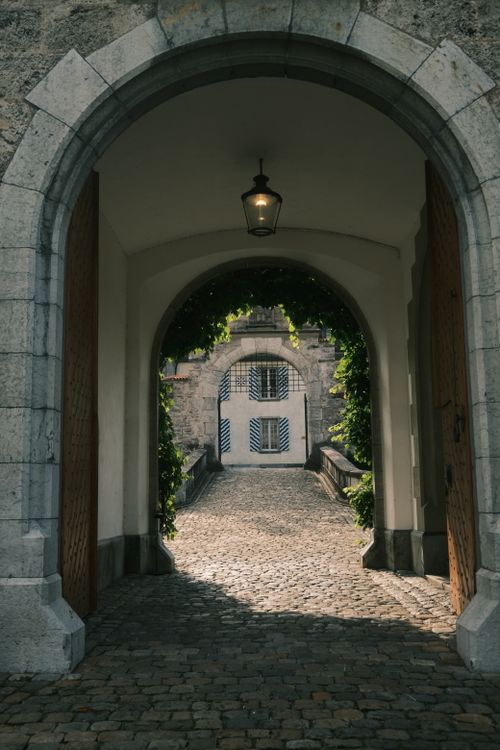 Free A captivating view through a stone archway leading to a cobblestone path and a historic building. Stock Photo