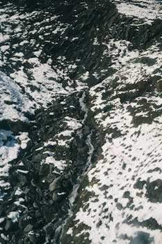 Aerial view of a snow-covered mountain landscape with a narrow rocky stream.