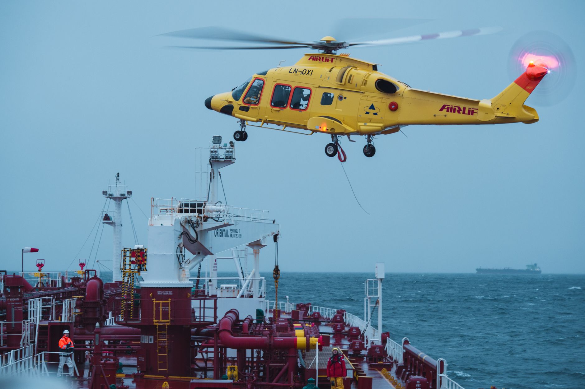 A yellow rescue helicopter performs a maritime operation over a cargo ship at sea.