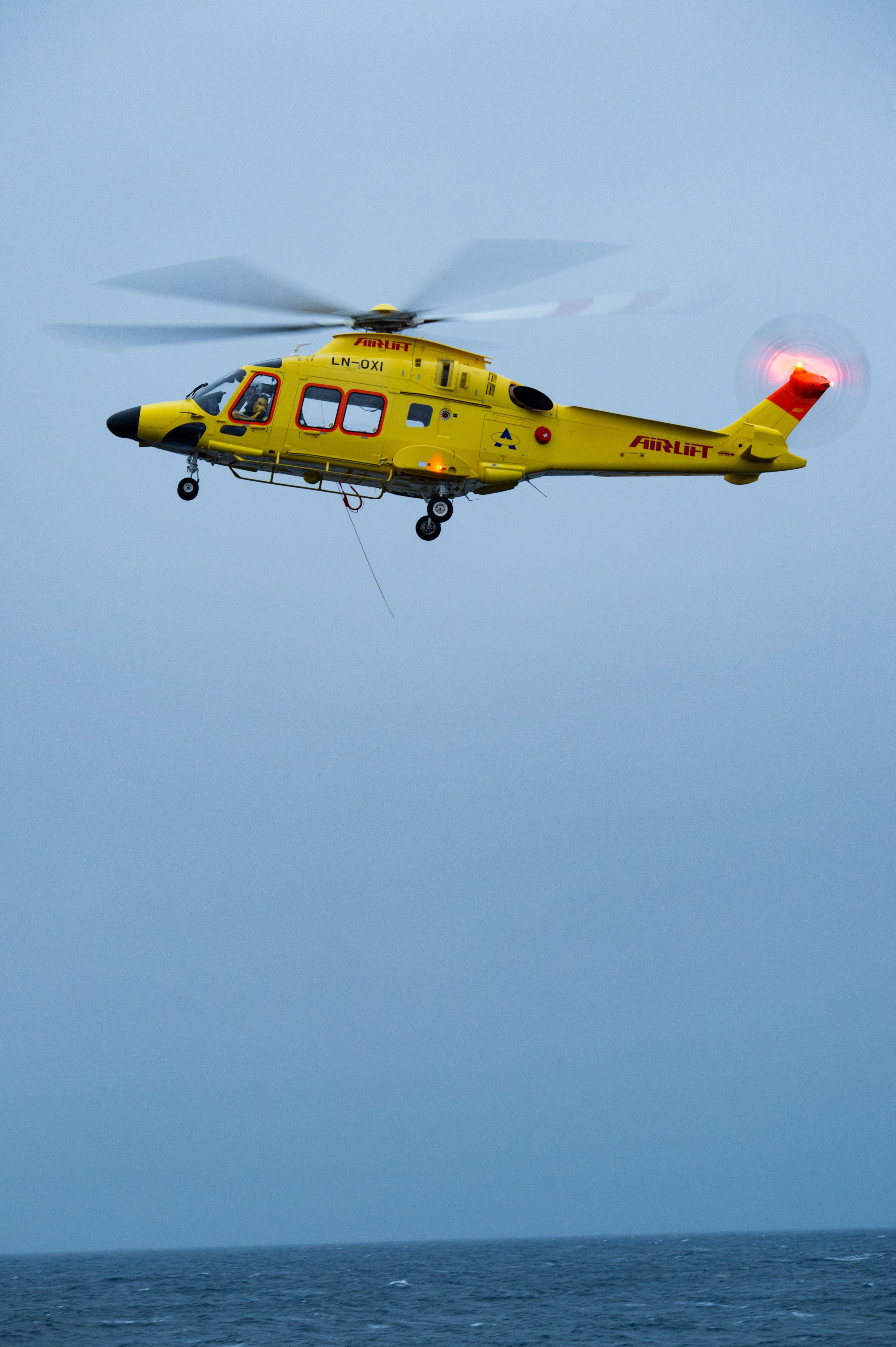 A yellow rescue helicopter in flight over a vast ocean, used for airlift operations.