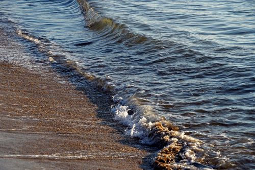 Free Gentle ocean waves roll onto a sandy beach at sunset, capturing a peaceful coastal scene. Stock Photo