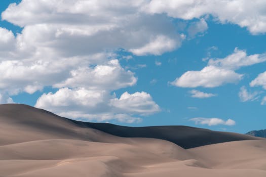 Stunning sand dunes landscape under a bright blue sky with fluffy clouds in Colorado, USA.