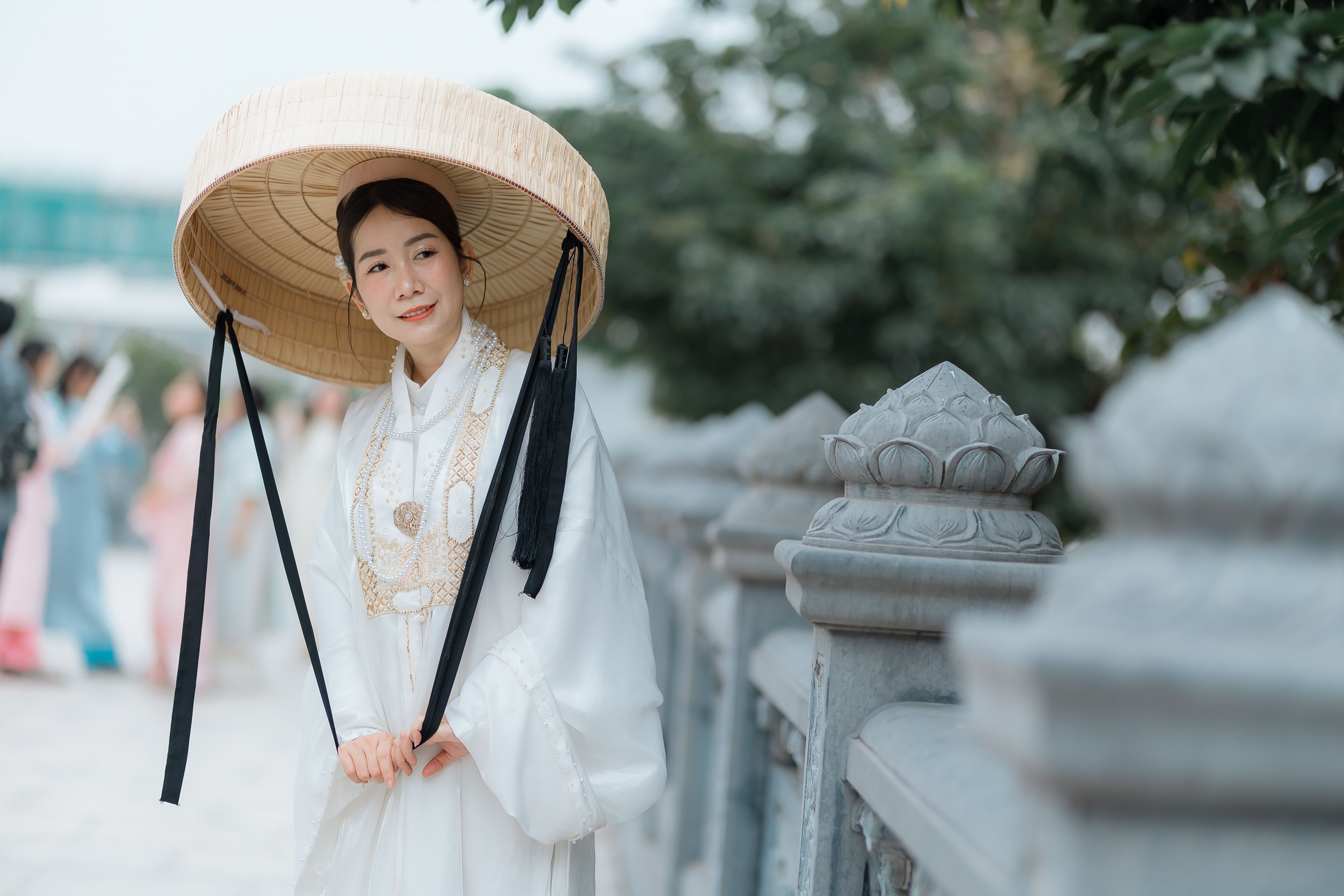 Asian woman in traditional attire with a bamboo hat outdoors, conveying cultural elegance.