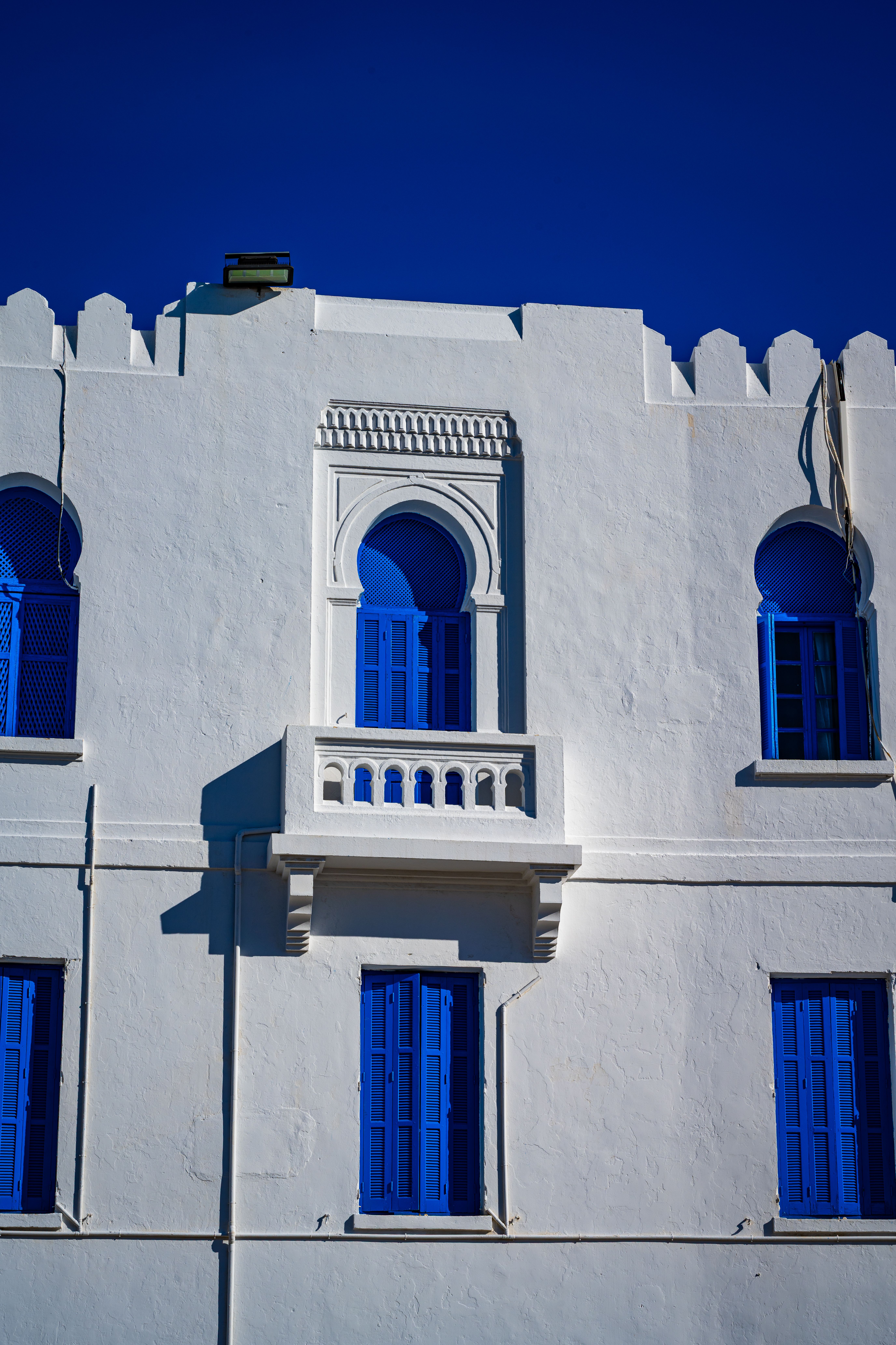 Elegant white building with blue windows in Tunisia featuring Islamic architectural style.