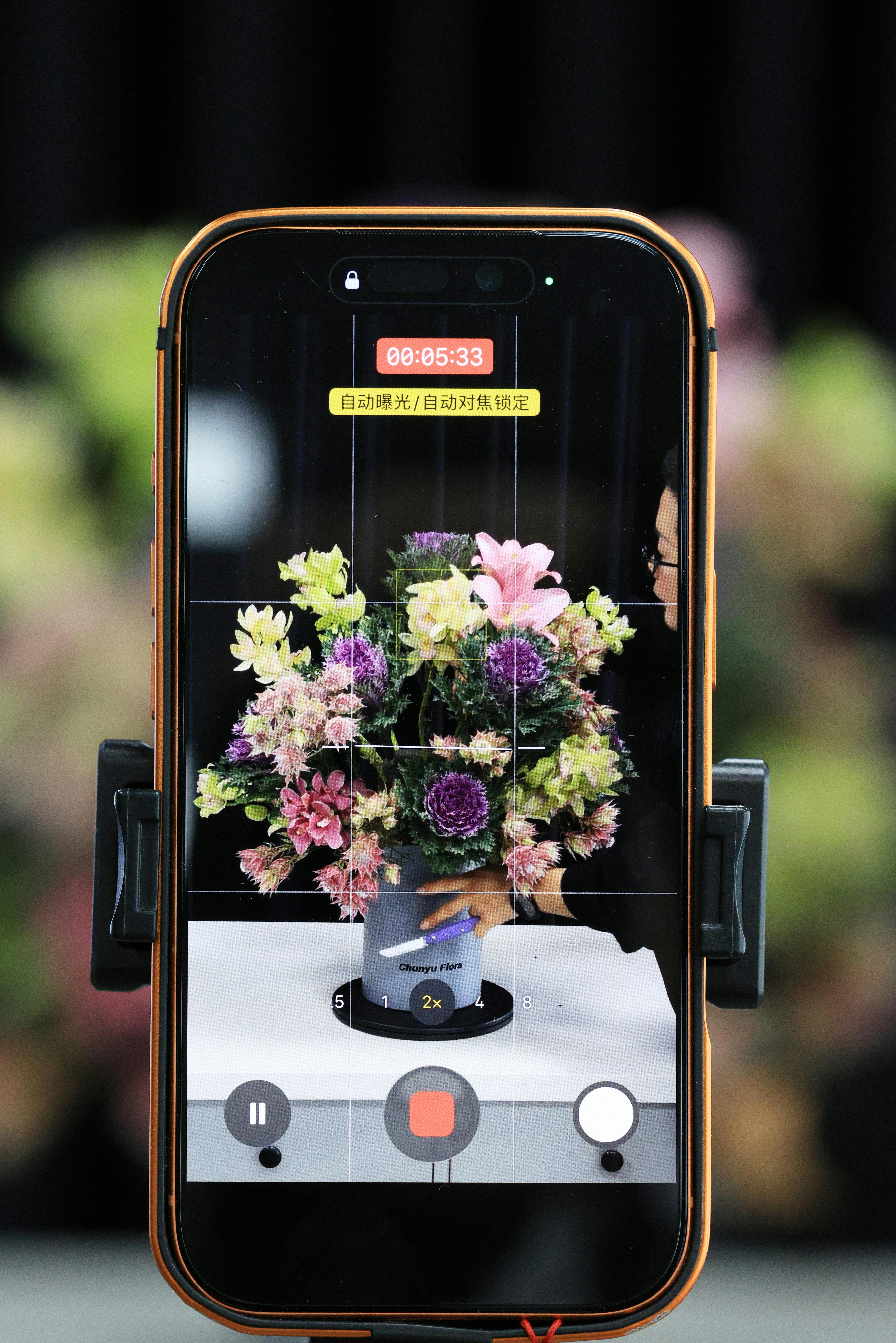 Free A smartphone filming a colorful flower bouquet on a stand, highlighting modern photography. Stock Photo