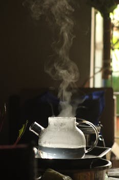Glass teapot releasing steam, creating a warm, cozy atmosphere indoors.