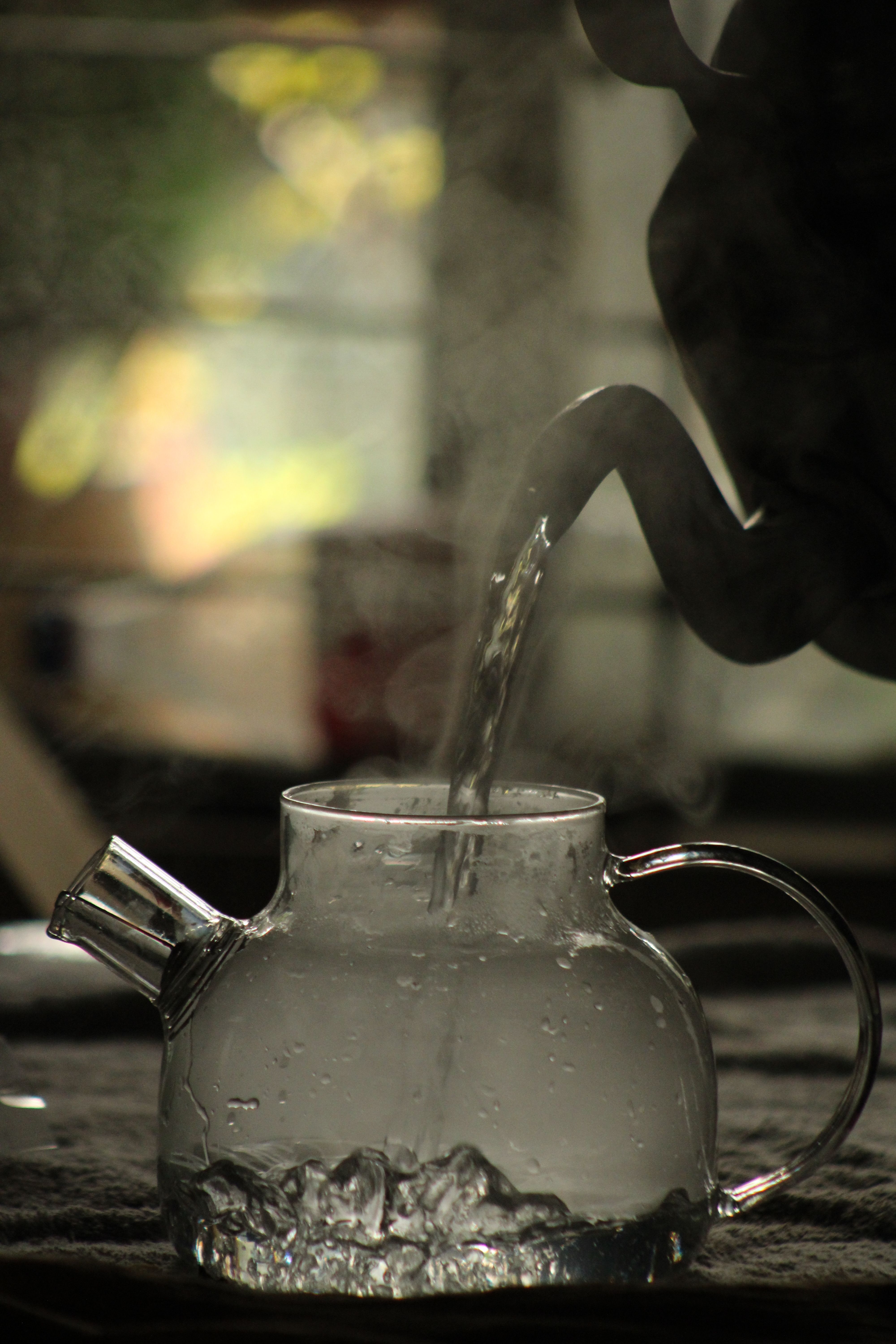 Steaming water being poured into a glass teapot with dramatic lighting.