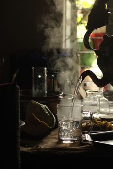 Steaming water being poured into a glass from a vintage kettle, creating a cozy indoor scene.