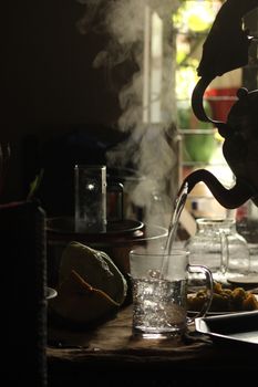 A warm, inviting setting of steam rising from tea being poured in dim light.