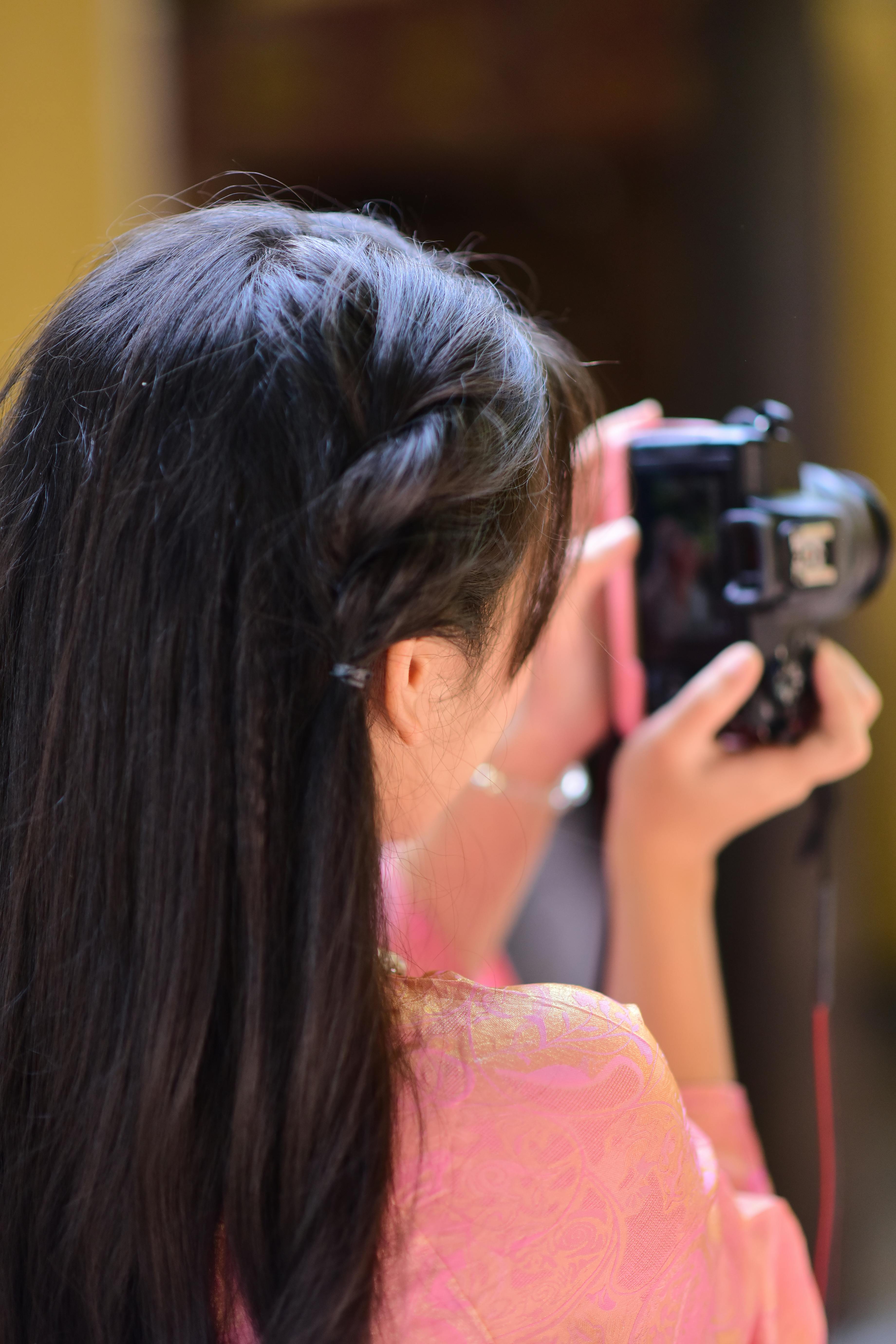 Free A woman with braided hair uses a DSLR camera for photography in an outdoor setting. Stock Photo