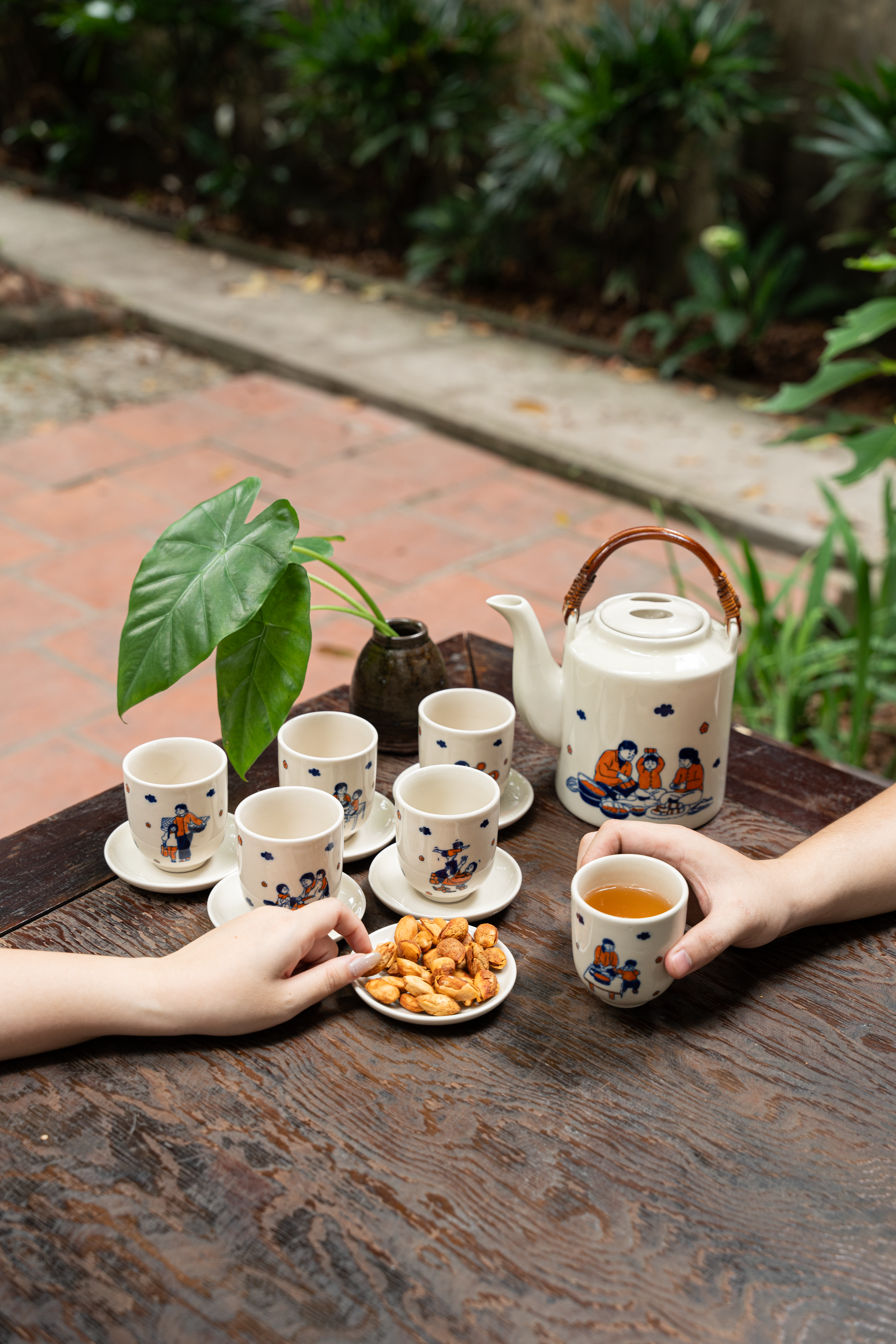 A traditional tea set with ceramic cups and teapot on a wooden table in a serene garden setting.