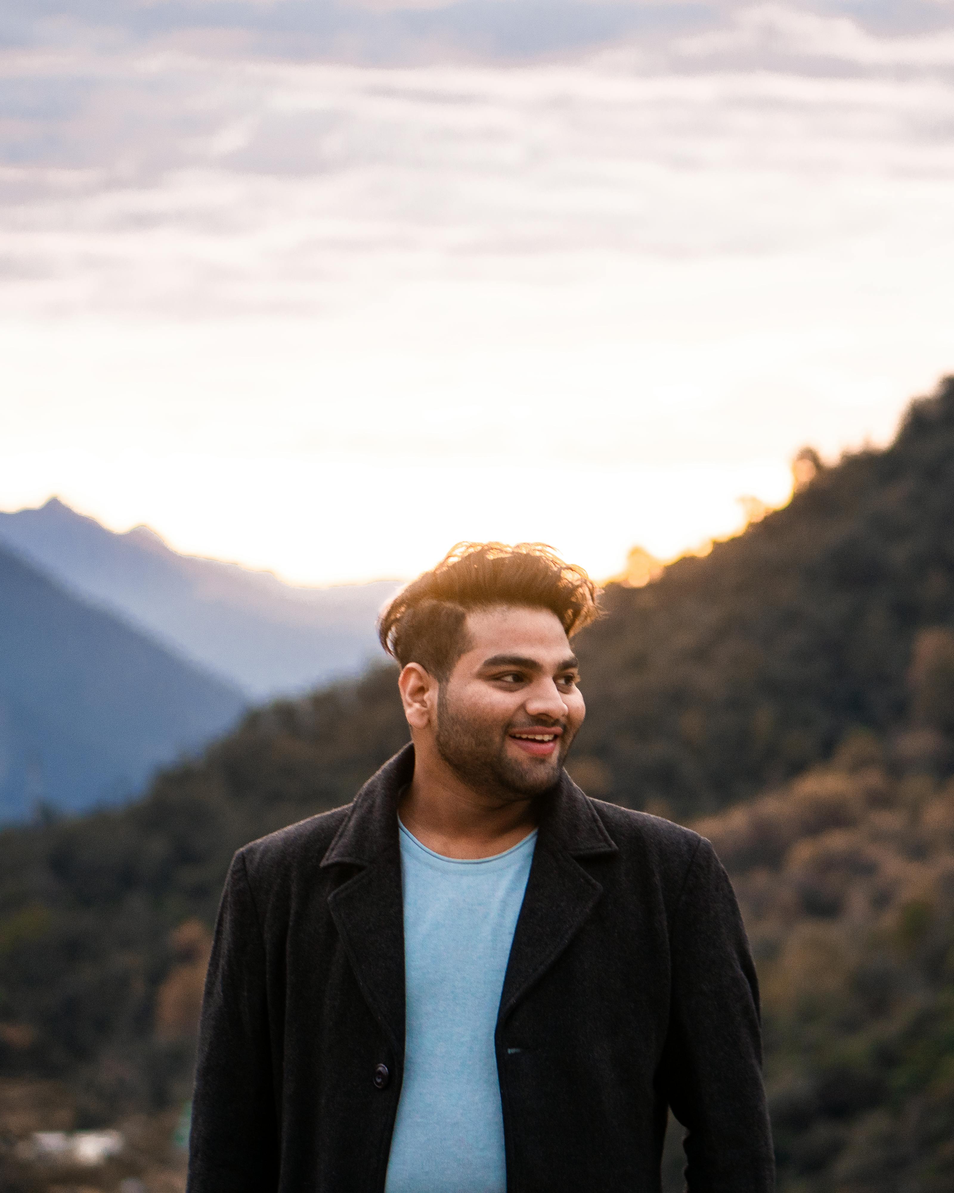 一个男人面带微笑站在户外，身后是群山和日出，洋溢着幸福与悠闲