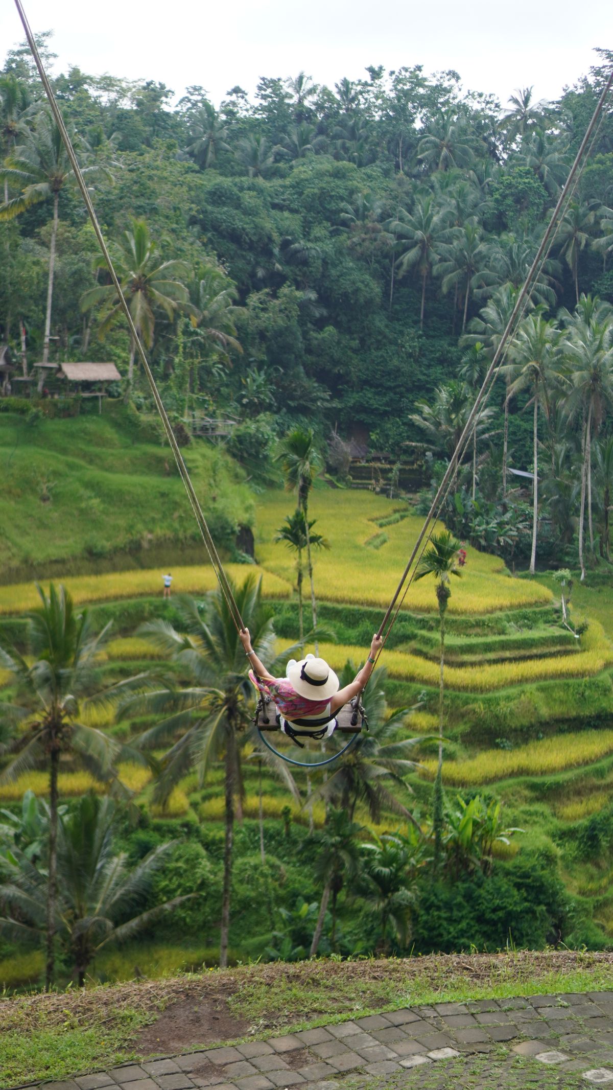 A woman in a sun hat on the Bali swing, swinging out over the green Tegalalang terraces