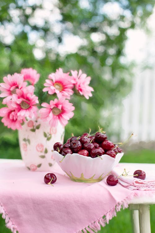 розовый цветок с лепестками рядом с бело зеленой чашей, полной вишни