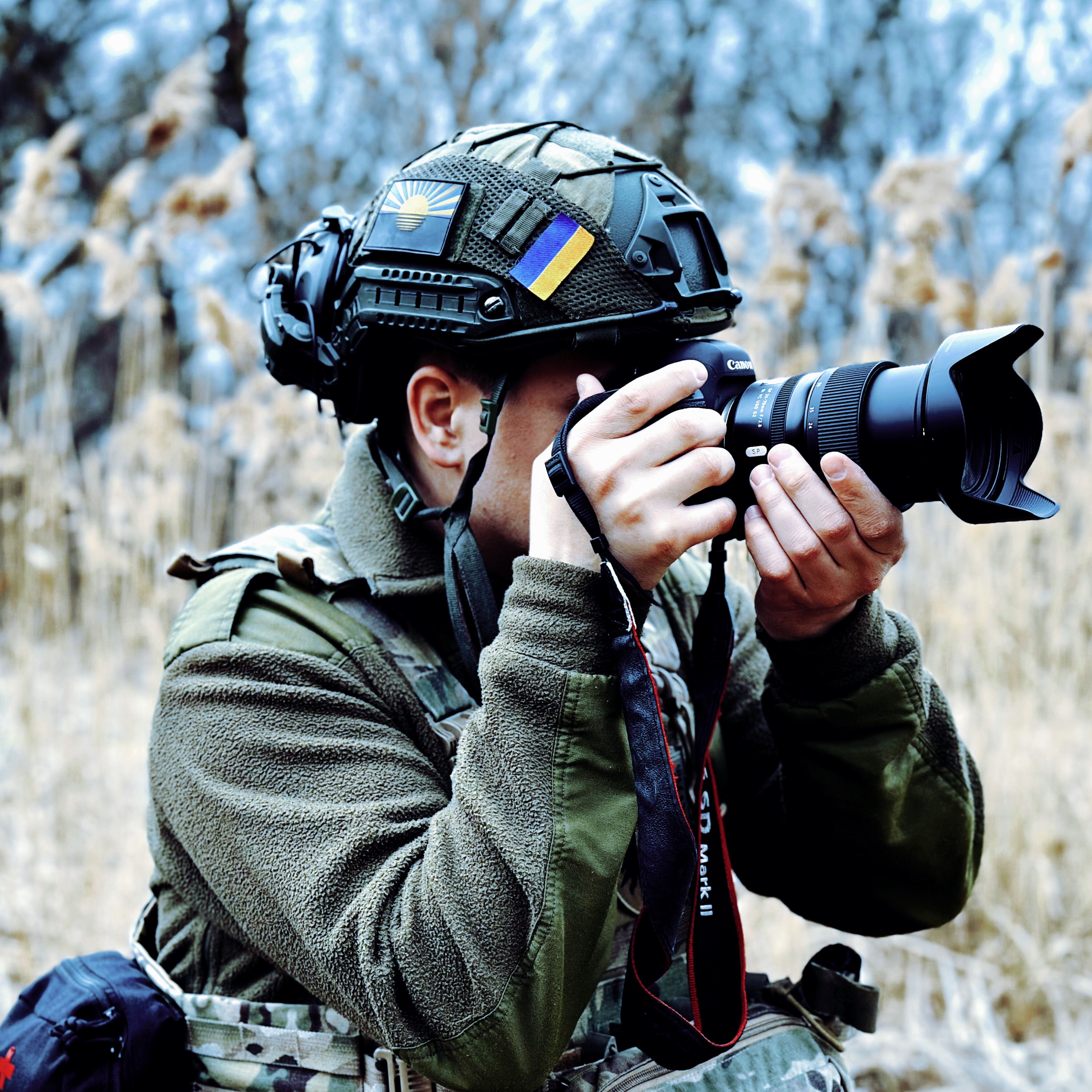 A soldier in full gear taking photos outdoors, showcasing military life.