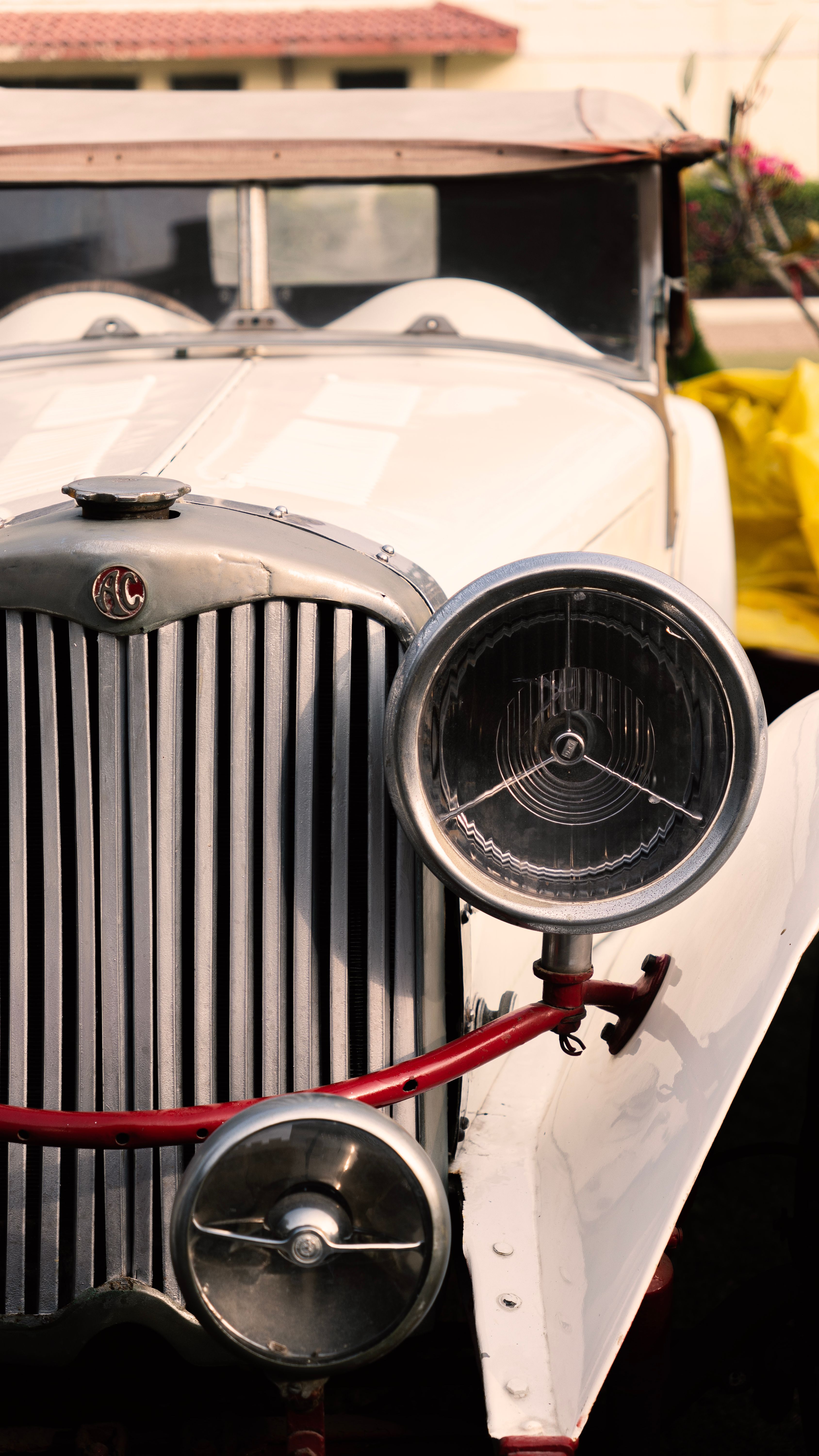 Close-up of a vintage white car featuring a unique headlamp and front grill design.