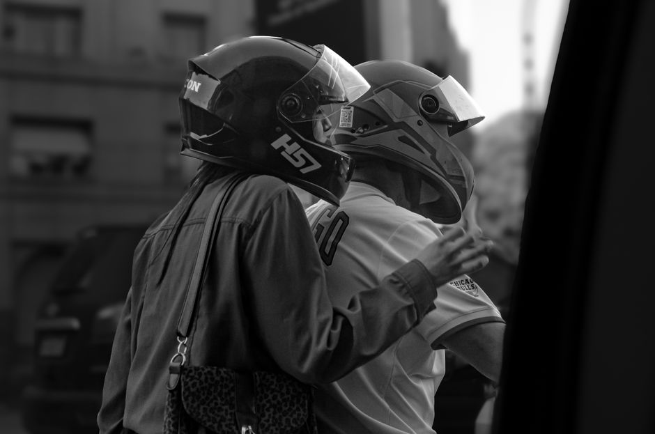 Two motorcyclists wearing helmets in a city captured in black and white.