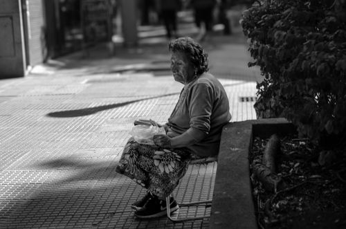 Free Black and white photo of an elderly woman sitting on a bench in an urban setting. Stock Photo